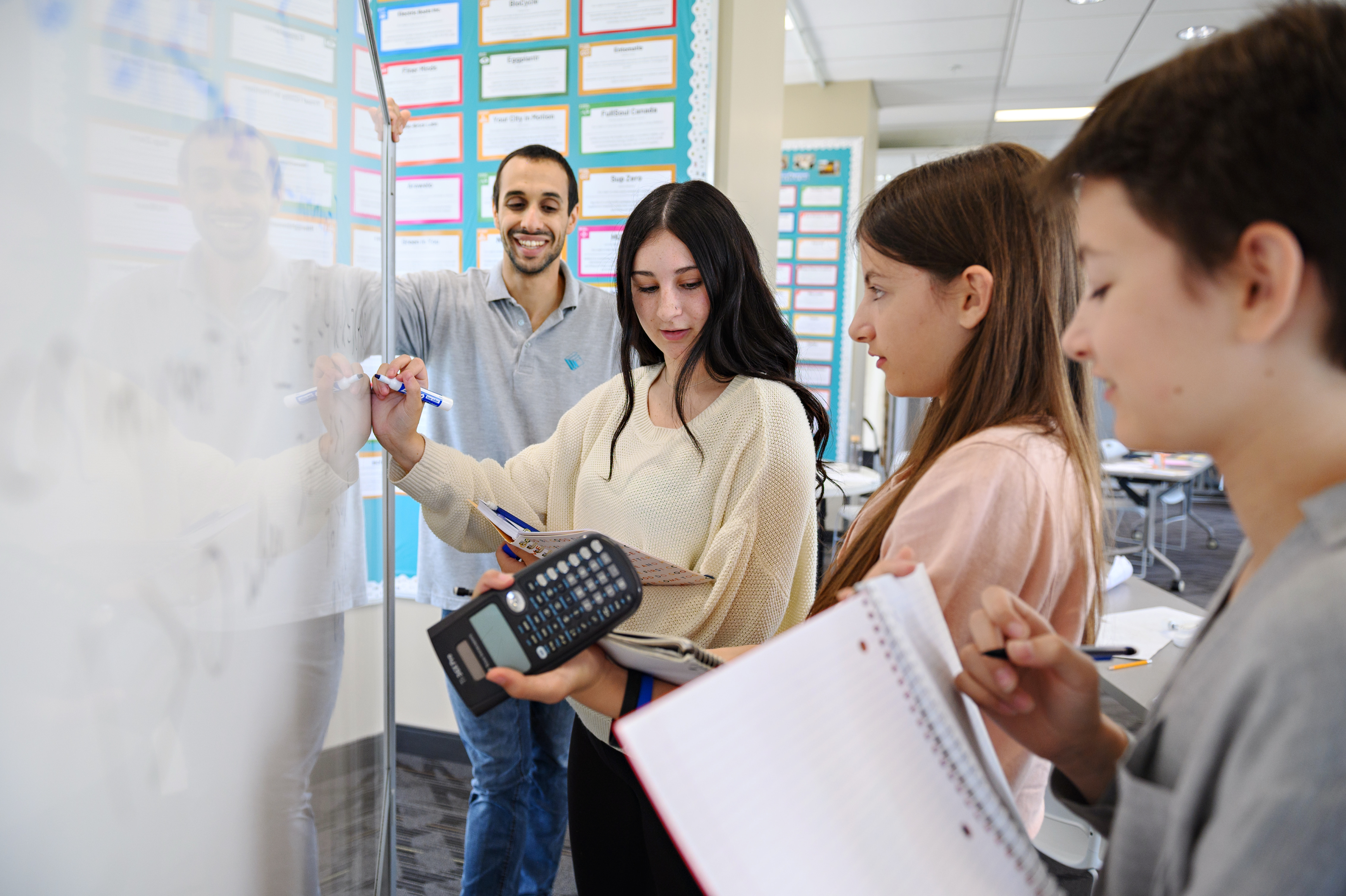 Students using a calculator and problem solving on a whiteboard along with their educator